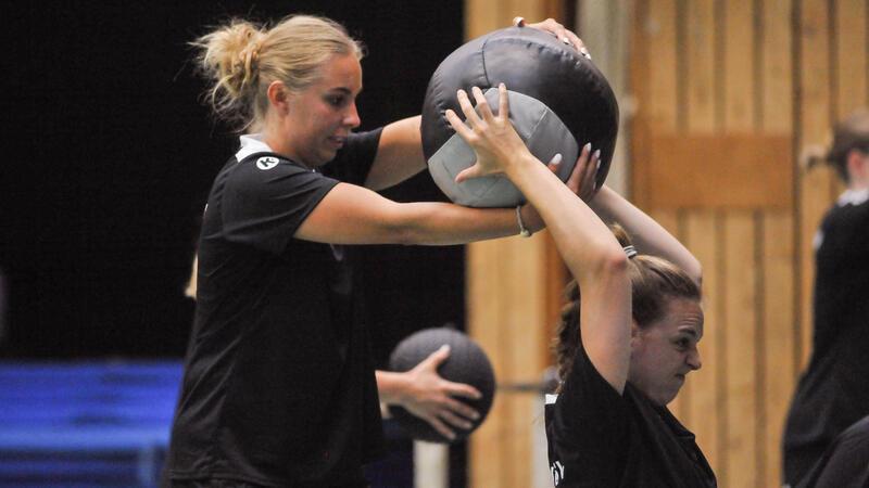 Oliwia Kaminska hilft Isabelle Dölle bei einer Kraftübung mit einem Ball.