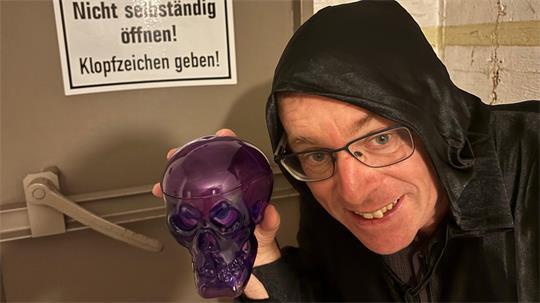 Mit Totenschädel-Skulptur in der Hand und im Kostüm wirbt VHS-Leiter Dirk Pohl vor der Bunkertür für den Besuch im gespenstisch gestalteten "Halloween-Bunker".