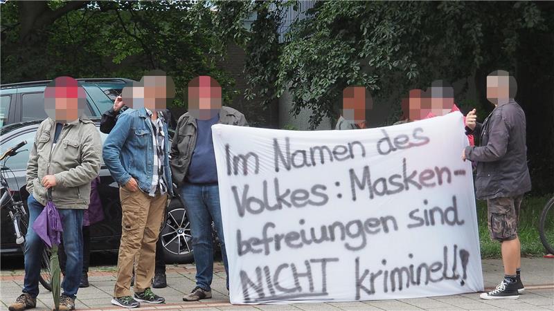 Falsche Corona-Atteste: Arzt vor Gericht – draußen Proteste Mit diesem Banner zeigte eine Gruppe von Demonstranten vor dem Amtsgericht ihre Gegnerschaft zur Maskenpflicht. Foto: Stehn