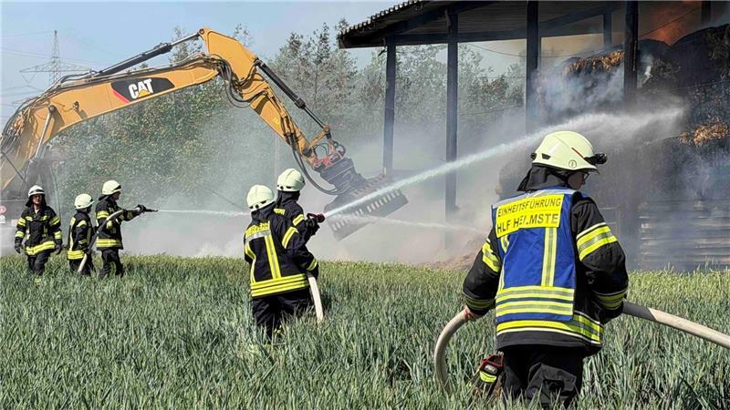 Großeinsatz für die Feuerwehr: Halle in Deinste steht in Flammen Mit einem Bagger werden die brennenden und kokelnden Stroh-Quaderballen auseinandergezogen.