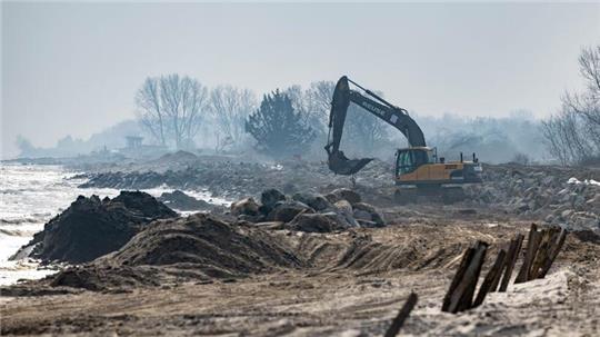 Mit einem Bagger werden grosse Steine am Strand am Hafen von Damp verladen.