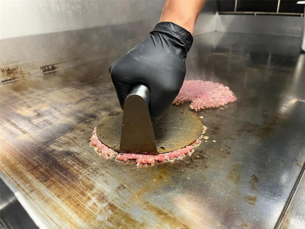 Mit einer Metallplatte werden die Burgerpatties "gesmasht".