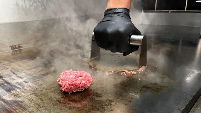 Mit einer Metallplatte werden die Fleischkugeln zu Patties "gesmasht".