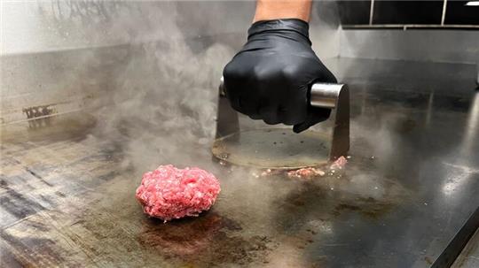 Mit einer Metallplatte werden die Fleischkugeln zu Patties "gesmasht".