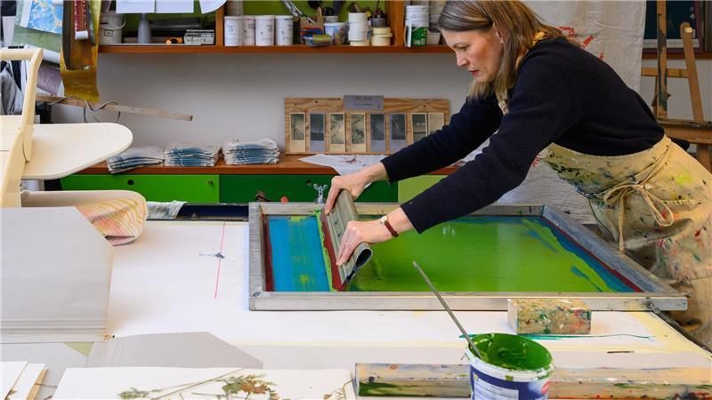 Mit einer Rakel verteilt Krieger die Farbe gleichmäßig auf dem Stoff.