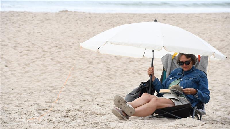 Hitzewelle im Norden: Zahlreiche Menschen strömen nach Sylt Mit ihrem Buch und einem Sonnenschirm genießt Urlauberin Kati Boetcher am Strand von Westerland die frische Meerbrise.
