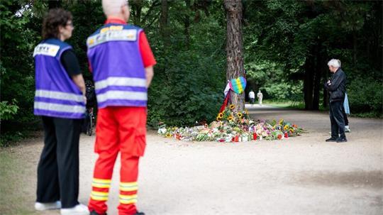Mitarbeitende des Kriseninterventionsteams und Trauernde stehen im Berliner Tiergarten an einem Baum, an dem Gegenstände zum Gedenken abgelegt wurden.