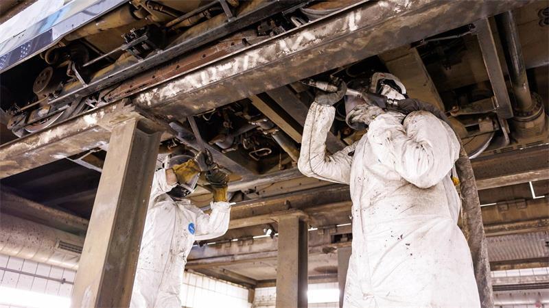 Mitarbeiter der Werkstatt der Verkehrsaktiengesellschaft VAG zeigen, wie ein Trockeneisstrahlgerät angesetzt werden muss, um ein durch Bitum verschmutztes Fahrwerks einer Straßenbahn zu reinigen (gestellte Szene). 