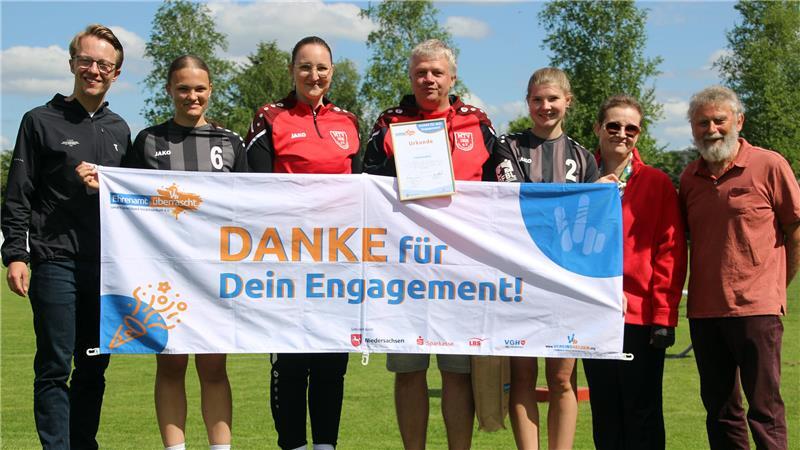 Vom Platzwart zum Vereinshelden: Ingo Lühmann geehrt Sechs Mitglieder des MTV Wangersen und Ingo Lühmann mit Urkunde in der Hand stehen hinter einem Banner mit der Aufschrift "Danke für Dein Engagement!".