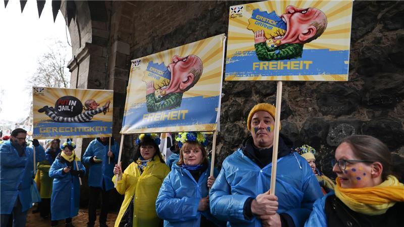 Mitglieder des ukrainischen Hilfsvereins Blau-Gelbes Kreuz halten im Kölner Rosenmontagszug Plakate mit früheren Putin-Darstellungen aus den Zügen in Köln und Düsseldorf hoch.