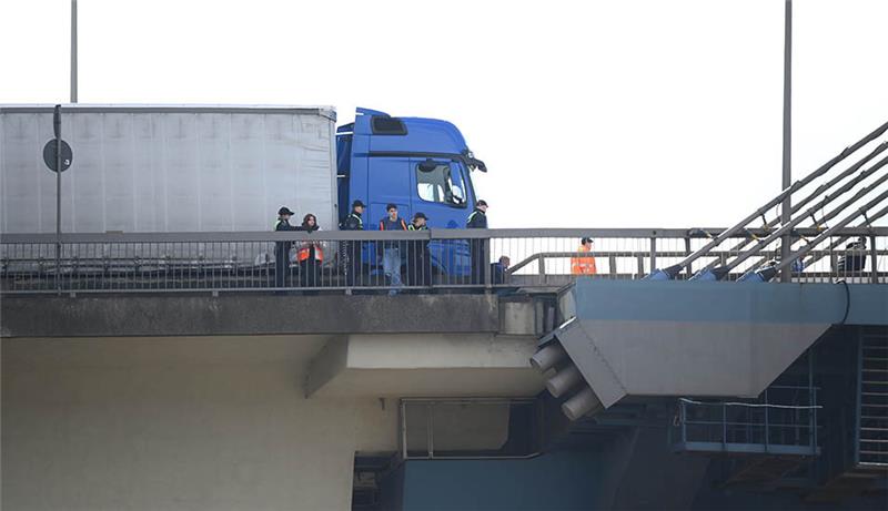 Mitglieder der Gruppe Letzte Generation und Polizisten stehen auf der Köhlbrandbrücke. Aktuell ist der Verkehr auf der Brücke durch eine Blockadeaktion zum Erliegen gekommen. Foto: Jonas Walzberg/dpa