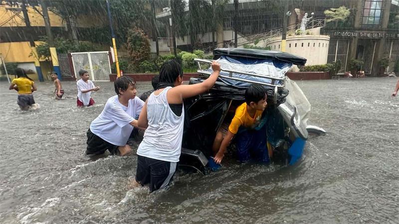 Monsunregen: Menschen schieben ein Dreirad-Taxi durch eine überflutete Straße auf den Philippinen.