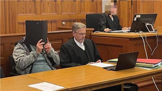 Mordprozess nach einer Gewalttat in Otterndorf: Im Gerichtssaal verbirgt der neben seinem Anwalt sitzende Angeklagte sein Gesicht hinter einem Aktendeckel.