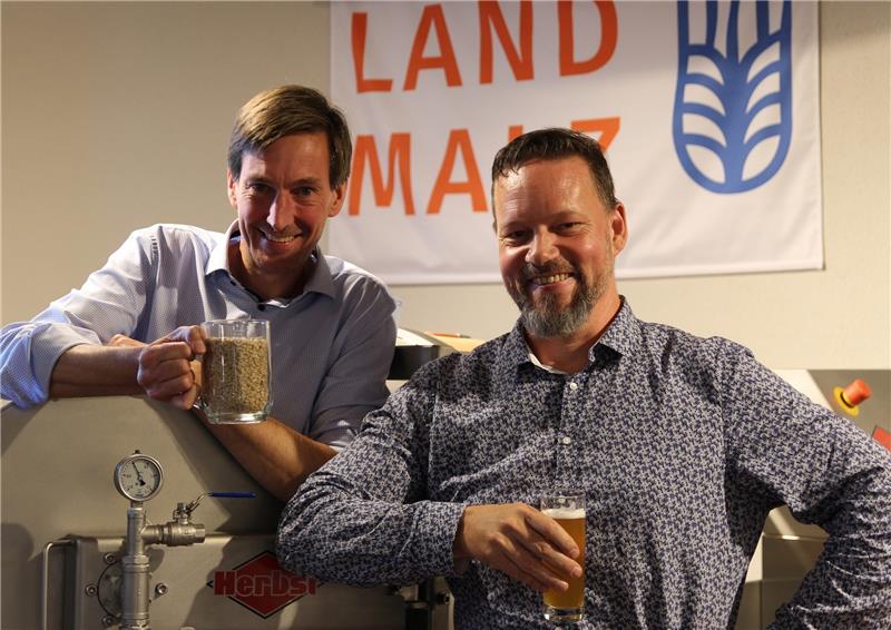 Moritz Bartmer hält ein Glas Gerste, Braumeister Marco Hacker ein Glas Bier. Dazwischen steht der Prototyp der patentierten Mälzanlage. Foto: Richter