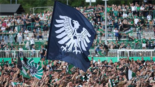 Münsters Fans haben das Spielfeld gestürmt und schwenken eine Fahne mit dem Preußen-Adler.