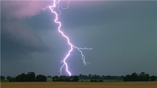 Ein Blitz leuchtet über einer Landschaft auf.
