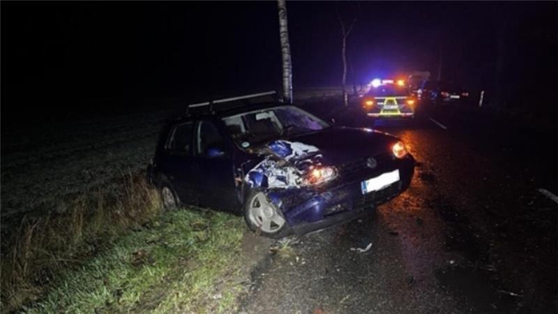 Betrunkener Pick-up-Fahrer tischt Polizei Lügengeschichte auf Man sieht ein am rechten Kotflügel beschädigtes Auto auf einer Straße. Im Hintergrund Polizei.