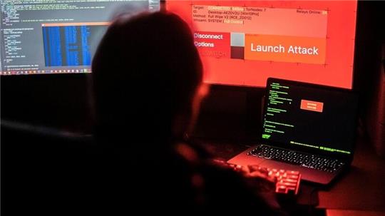 Ein Mann sitzt vor Bildschirmen, die Hacker-Programme und eine fiktive Fernlösch-Software (Wiper) zeigen .