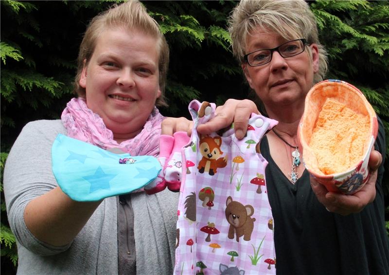 Nähen und Basteln für Frühchen und Sternenkinder : Wiebke Müller (links) und Melanie Hesse-Völkner zeigen ein Pucksäckchen, Erinnerungsperlen und Strampler. In das genähte Körbchen können Eltern ihre totgeborenen Kinder betten. Foto Klempow