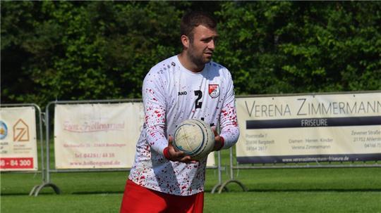 Nick Poppe vom MTV Wangersen mit weißem Langarmshirt und roter Hose hält einen Faustball in der Hand.