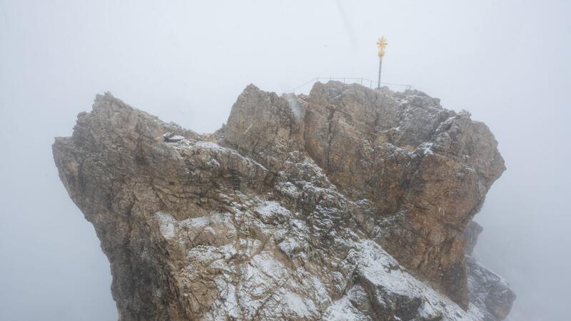 Bergnot: Bergsteiger im Schneetreiben an Zugspitze gerettet Nebelwolken umhüllen bei Schneetreiben auf der Zugspitze die Aussichtsplattform mit dem Gipfelkreuz (Archivbild). Aus mehreren Bergsteigergruppen wurden Notrufe abgesetzt, nachdem sie aufgrund von Witterung und Neuschnee auf etwa 2500 Metern Höhe nicht mehr weiterkamen.