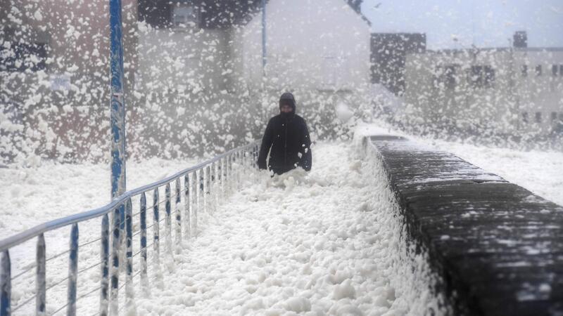 Nein, das sind keine dicken Schneeflocken. Es handelt sich um Meeresschaum, der von einem Sturm an eine Küste gespült wird.