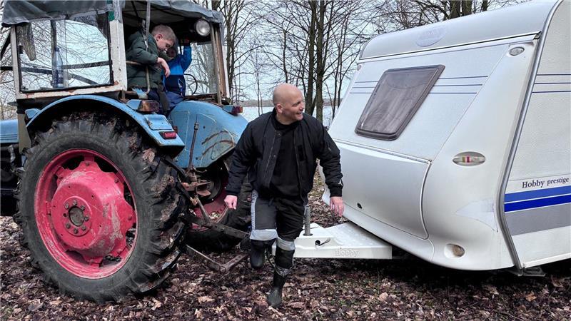 Neu-Camper Brian Zaremba aus Hamburg weist den Treckerfahrer ein, im Hintergrund die Fahrrinne der Elbe.