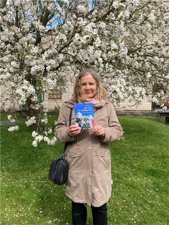 Nicht im Alten Land, sondern auf einem alten Hof an der Weser: Christa Picard mit ihrem neuen Buch vor einem blühenden Apfelbaum. Foto: Picard