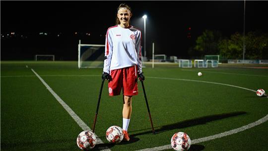 Nicola Roos, Amputierten-Fußballerin des 1. FSV Mainz 05, steht bei einem Training auf dem Sportplatz der Spielvereinigung Essenheim neben Fußbällen.