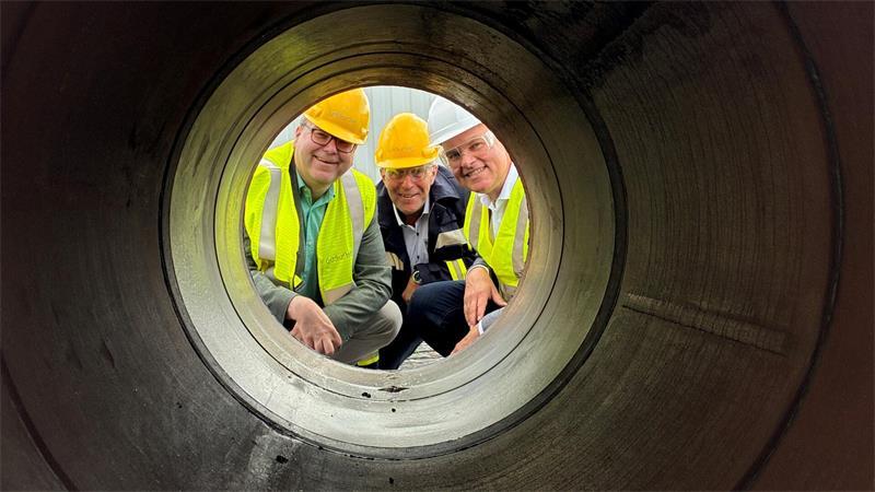 Niedersachsens Energieminister Christian Meyer blickt mit Bürgermeister Timo Gerke und Schleswig-Holsteins Energiewendeminister Tobias Goldschmidt auf Lühesand auf der Baustelle der Gasunie-Hyperlink-Wasserstoffpipeline durch ein Rohr (von links).