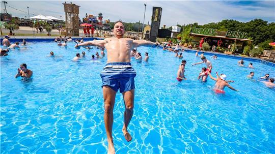 Niklas H.aus Heideburg in Rheinland-Pfalz springt bei sommerlichen Temperaturen rückwärts in den großen Pool auf dem Festivalgelände.