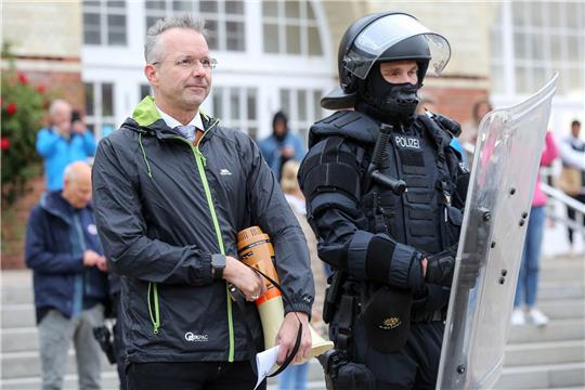 Nikolas Häckel, Bürgermeister der Gemeinde Sylt (l, parteilos) stand am 14. September 2019 während der freiwilligen Räumung des Punk-Protestcamp in Westerland auf Sylt neben einem Polizisten in Schutzausrüstung. Im vergangenen Jahr hatten Punks Protestcamps auf Sylt errichtet. Foto: Bodo Marks/dpa