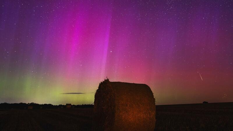 Polarlichter und Sternschnuppen am Nachthimmel Nordlichter am Himmel, während eine Sternschnuppe über einem Strohballen am Himmel verglüht.