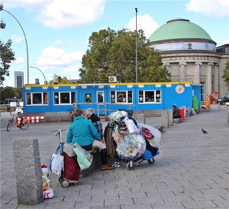 Obdachlose sitzen mit all ihren Habseligkeiten vor dem blauen Container der Bahnhofsmission am Hauptbahnhof Hamburg. Foto: Gehm