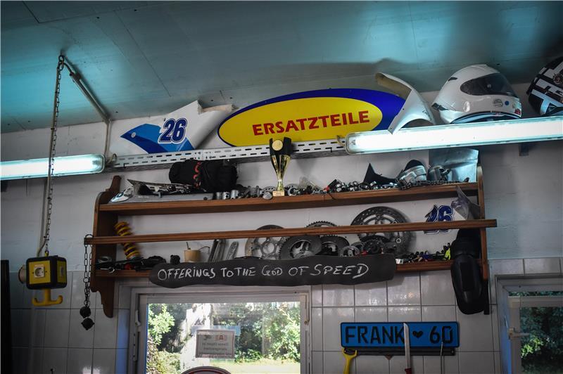 Ein Holzregal mit Ersatzteilen und einem Schild. Auf dem steht: „Offerings to the God of Speed.“