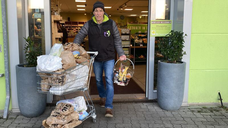 Olaf Ruser kommt mit einem Einkaufswagen voll mit Brottüten und einem zusätzlichen Einkaufskorb aus der Tür des Erdkorn Biomarktes