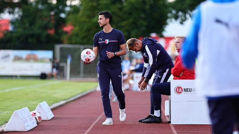 Bei D/A-Sieg: Wulffs Podcast-Prophezeiung wird wahr Oliver Ioannou steht an der Seitenlinie auf einer Tartanbahn mit Ball in der Hand.