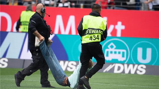 Ordner tragen bei einem Fußballspiel Demonstrierende vom Feld. Am heutigen Montag kann man sich als Sicherheitskraft für die Fußball-EM bewerben.