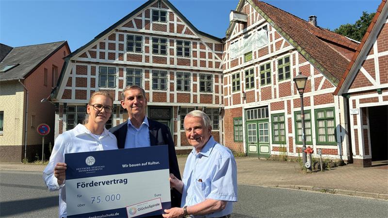 Ortskurator Dr. Reinhold Kolck (rechts) von der Deutschen Stiftung Denkmalschutz überreicht Inga und Jan Thesing den symbolischen Fördervertrag vor ihrem Haus am Fleet 14 (links).