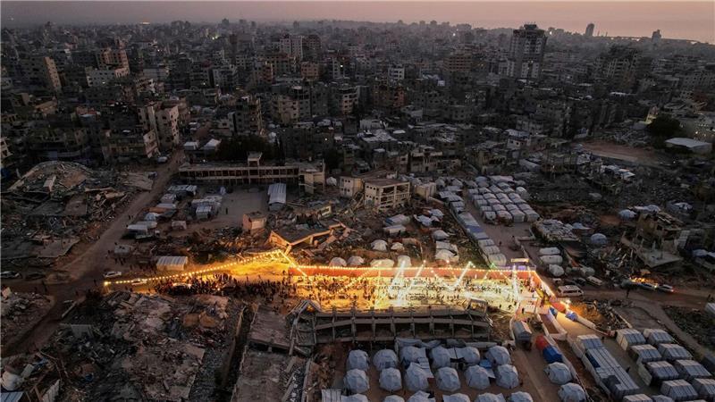 Palästinenser sitzen an einem großen Tisch, umgeben von Zelten und den Trümmern zerstörter Häuser und Gebäude, während sie sich zum Iftar, dem Fastenbrechen, während des Ramadan versammeln.