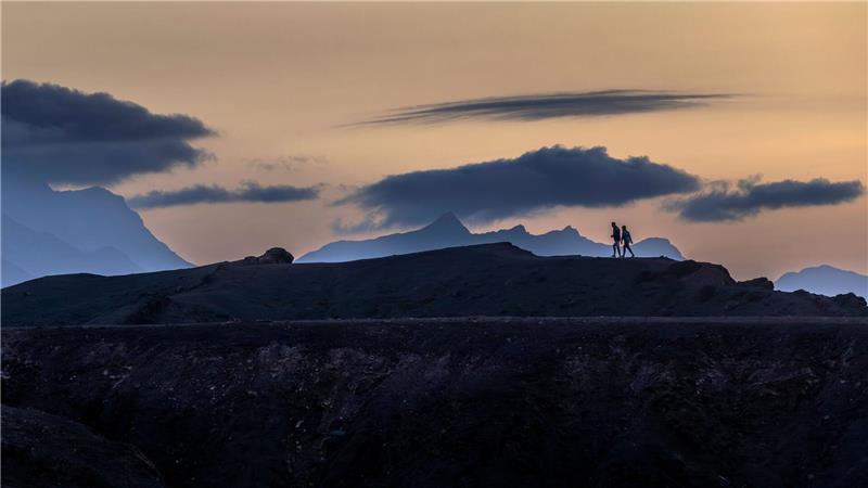 Panodrama: Menschen gehen auf der Insel Fuerteventura unter dramatisch wirkenden Wolkenformationen.