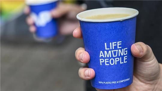 Pappbecher mit Kaffee und dem Logo der Kette „Lap Coffee“. Die Abkürzung steht für „Life Among People“. 