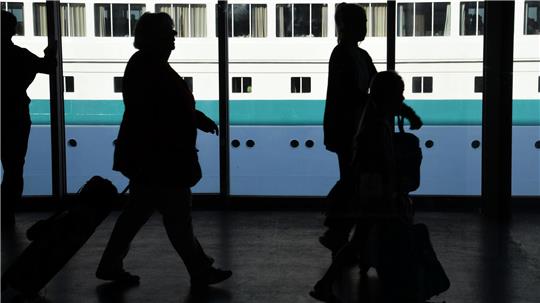 Passagiere gehen durch das Kreuzfahrtterminal mit Gepäck an Bord ihres Schiffes. Foto: Jaspersen/dpa