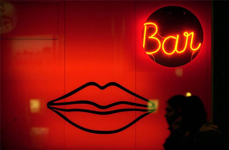 Passanten gehen an einer Erotik-Bar vorbei, die im rot beleuchteten Schaufenster mit übergroßen Lippen wirbt. Foto: Arne Dedert/dpa
