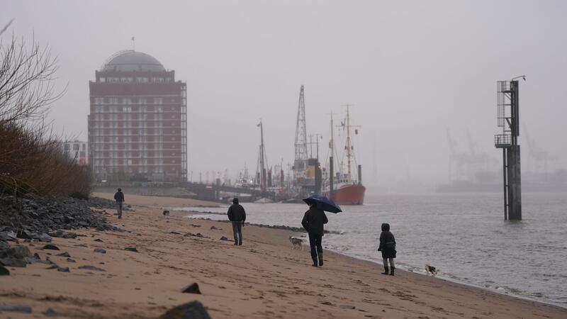 Passanten gehen im strömenden Regen am Elbstrand in Ovelgönne spazieren.