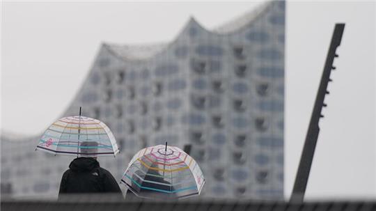 Passanten gehen im strömenden Regen auf der Jan-Fedder-Promenade im Hamburger Hafen spazieren.