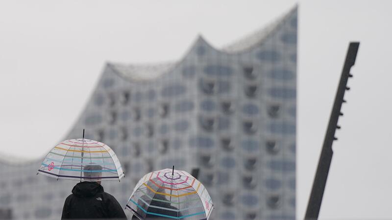 Passanten gehen im strömenden Regen auf der Jan-Fedder-Promenade im Hamburger Hafen spazieren.