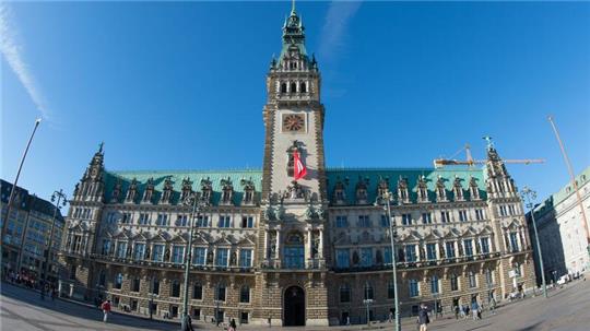 Passanten gehen in Hamburg bei strahlendem Sonnenschein über den Rathausmarkt.