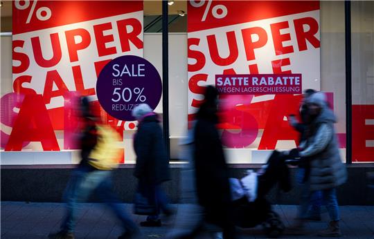 Passanten gehen in der Innenstadt an einem Schaufenster vorbei mit Plakaten zum "Super Sale". Foto: Christian Charisius/dpa