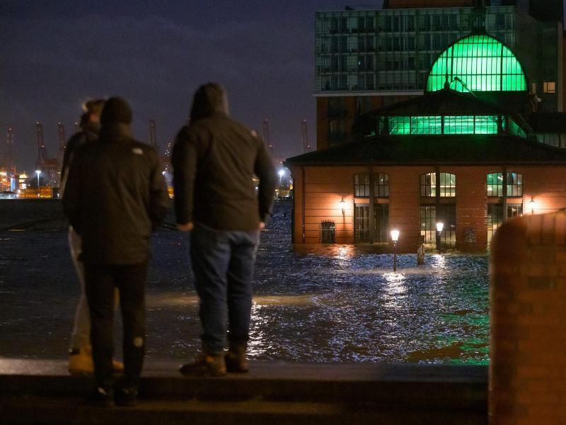 Passanten stehen am frühen Morgen vor dem überfluteten Hamburger Fischmarkt. Foto: Jonas Walzberg/dpa